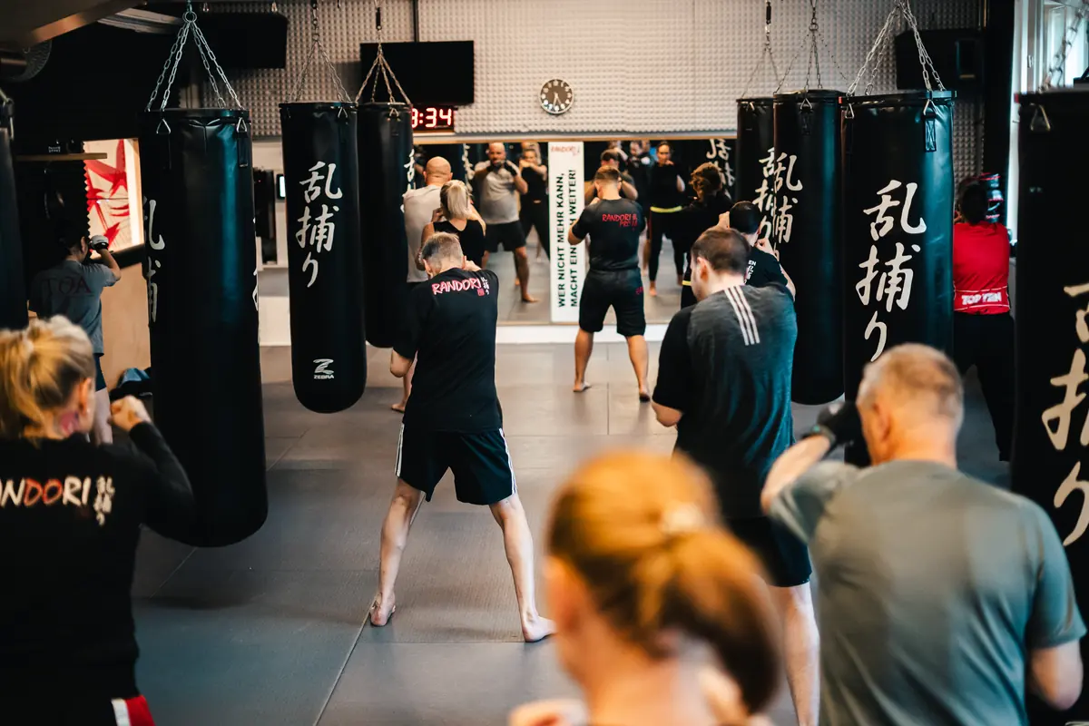 Fitness Boxen: Mehrere Erwachsene trainieren mit Boxhandschuhen an einer Reihe von Sandsäcken