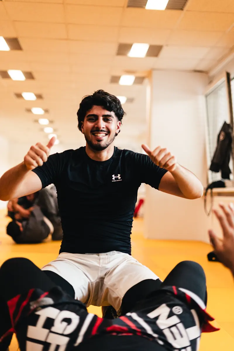 Grappling: Sportler sitzt lachend auf der Matte und zeigt beide Daumen nach oben