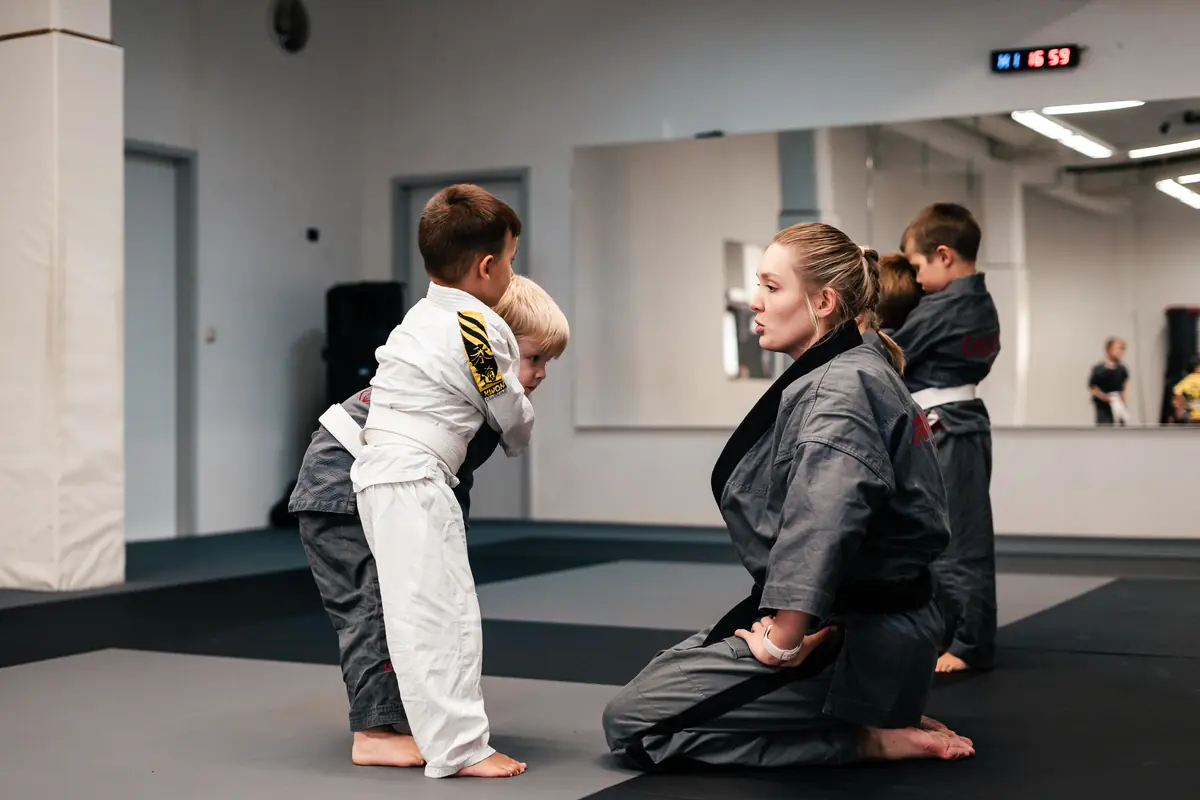 Randori-Pro Waltersdorf: Eine Frau im Gi kniet auf der Matte und übt mit zwei Kindern