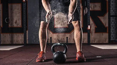Kettlebell-Training: Hände mit Magnesia über einer Kettlebell am Boden