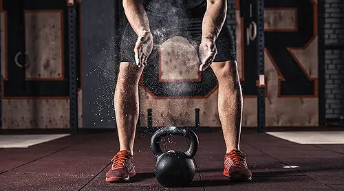Kettlebell auf dem Boden, darüber reibt sich ein Sportler Magnesia in die Hände