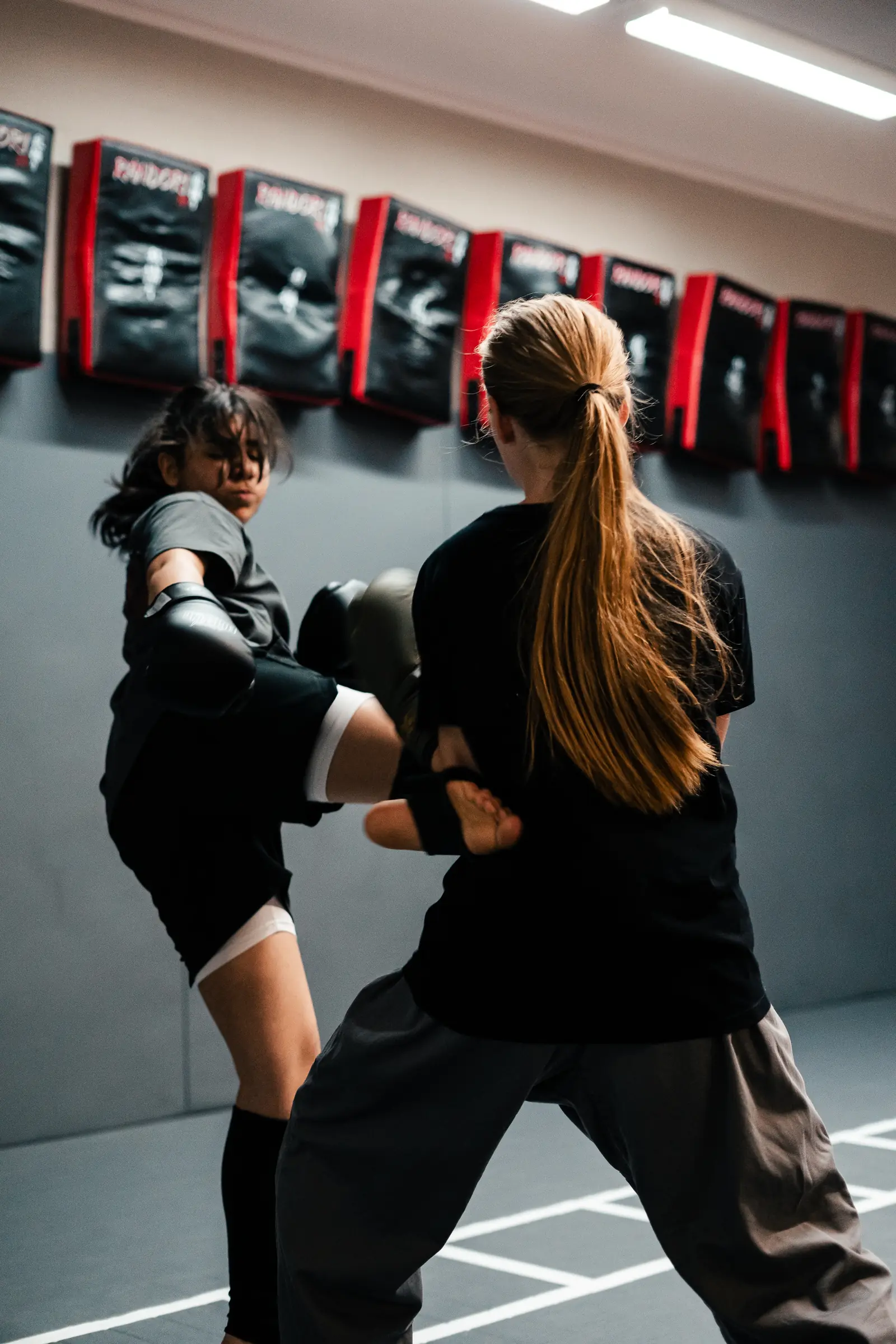 Kickboxen für Kinder bei Randori-Pro: Eine Jugendliche mit Boxhandschuhen setzt einen Tritt, ihre Trainingspartnerin nimmt ihn an