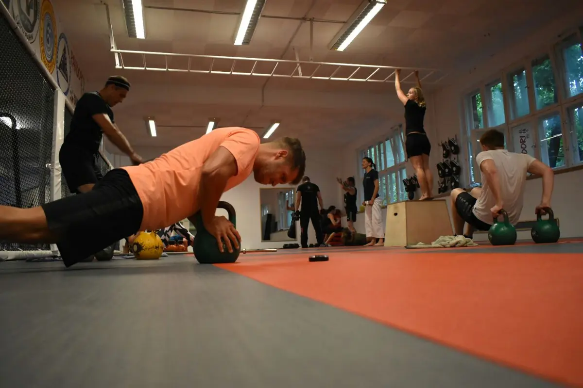 Kraftzirkel: Ein Teilnehmer macht Liegestütze auf Kettlebells, im Hintergrund trainiert die Gruppe