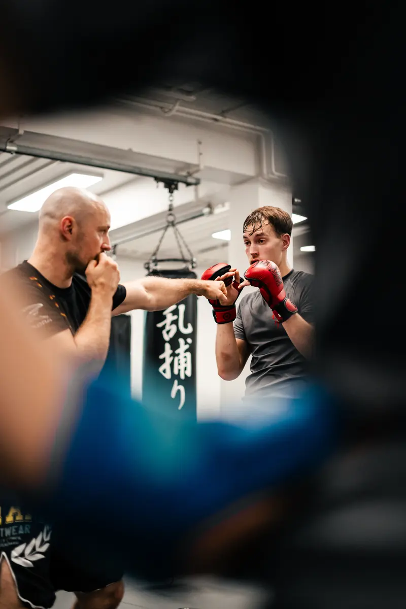 MMA-Training: Partnerübung im Stand, ein Sportler mit MMA-Handschuhen wehrt einen Schlag ab