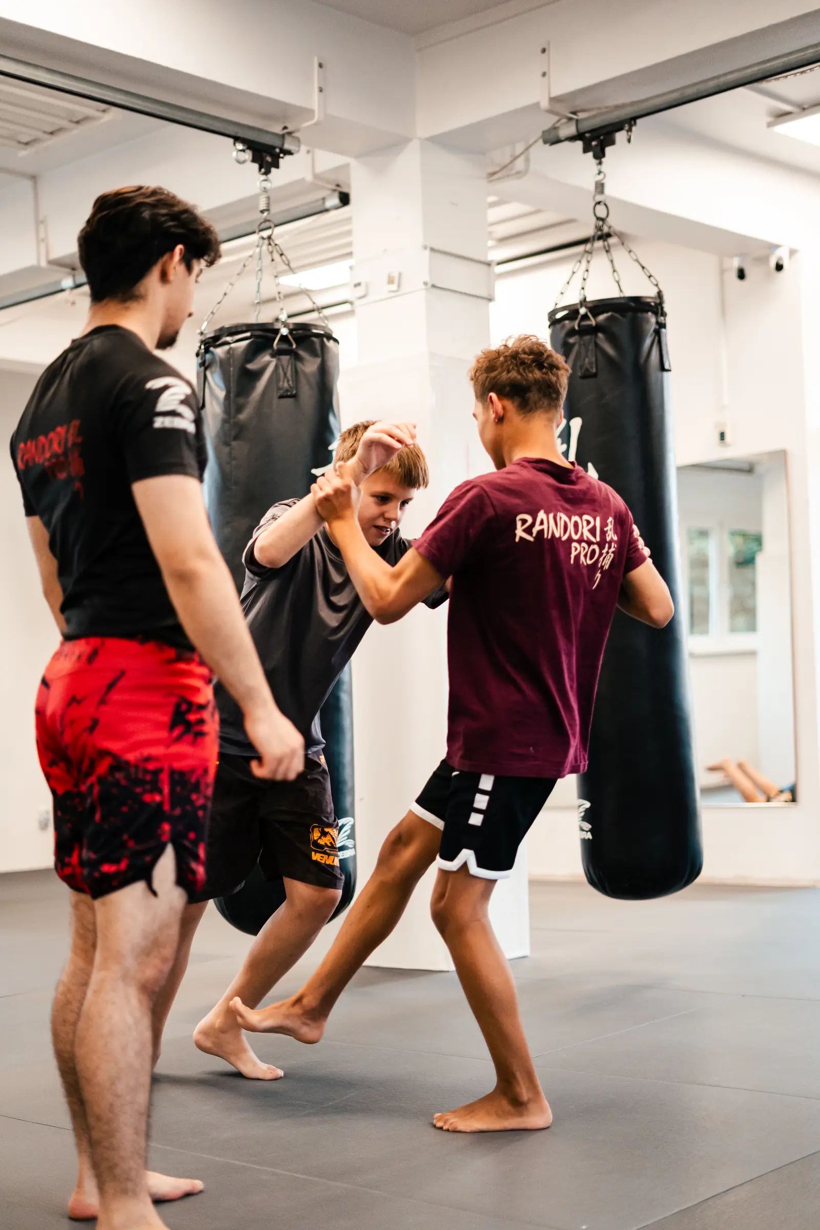 MMA für Kinder bei Randori-Pro: Zwei Jungen üben einen Griff im Stand, ein Trainer schaut zu
