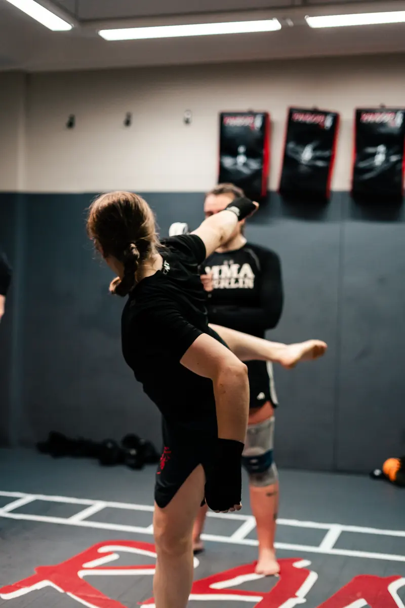 Kickbox-Training: Eine Frau setzt einen Tritt an, ein Trainingspartner steht vor ihr