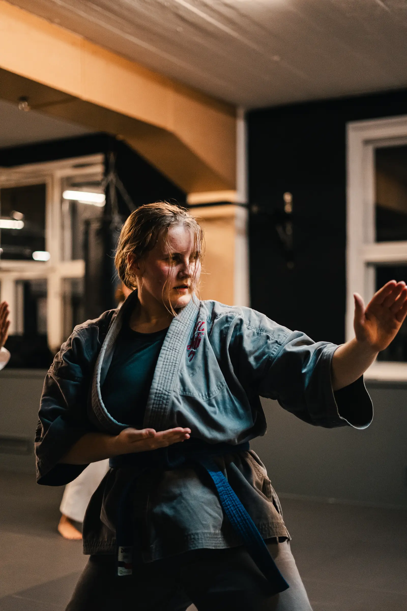 Eine Karateka im Gi mit blauem Gürtel in konzentrierter Abwehrhaltung
