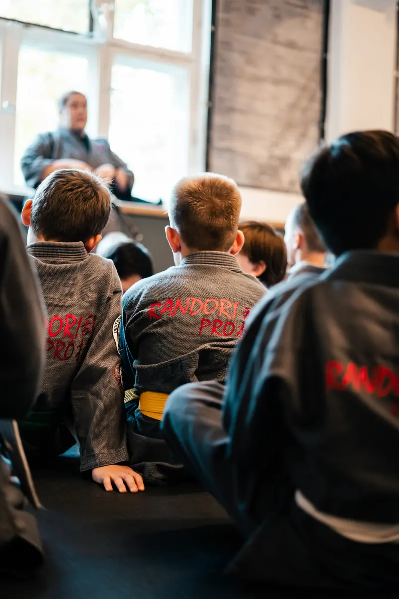 Kinder im Kampfanzug sitzen auf der Matte und hören einem Trainer zu