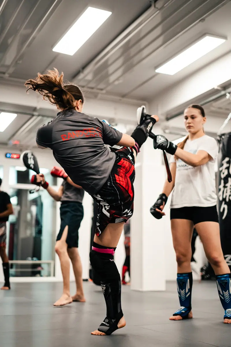 MMA-Training: Eine Frau tritt hoch auf die Pratze ihrer Trainingspartnerin