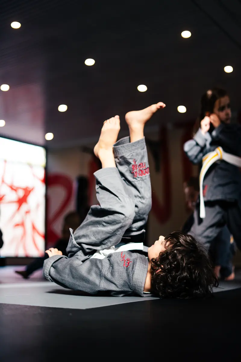 Jiu-Jitsu Kinder-Training bei Randori-Pro — Kind im Gi liegt bei einer Übung auf dem Rücken und streckt die Beine in die Luft