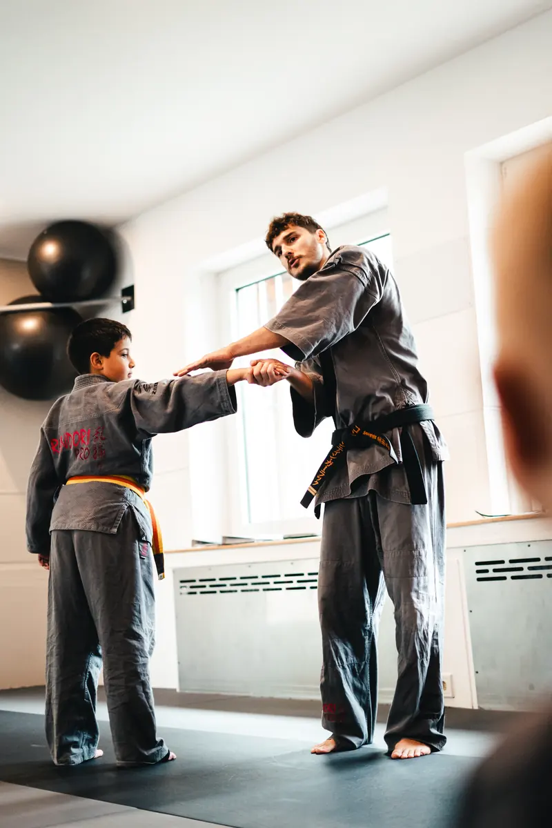 Trainer im Gi übt mit einem Jungen eine Technik